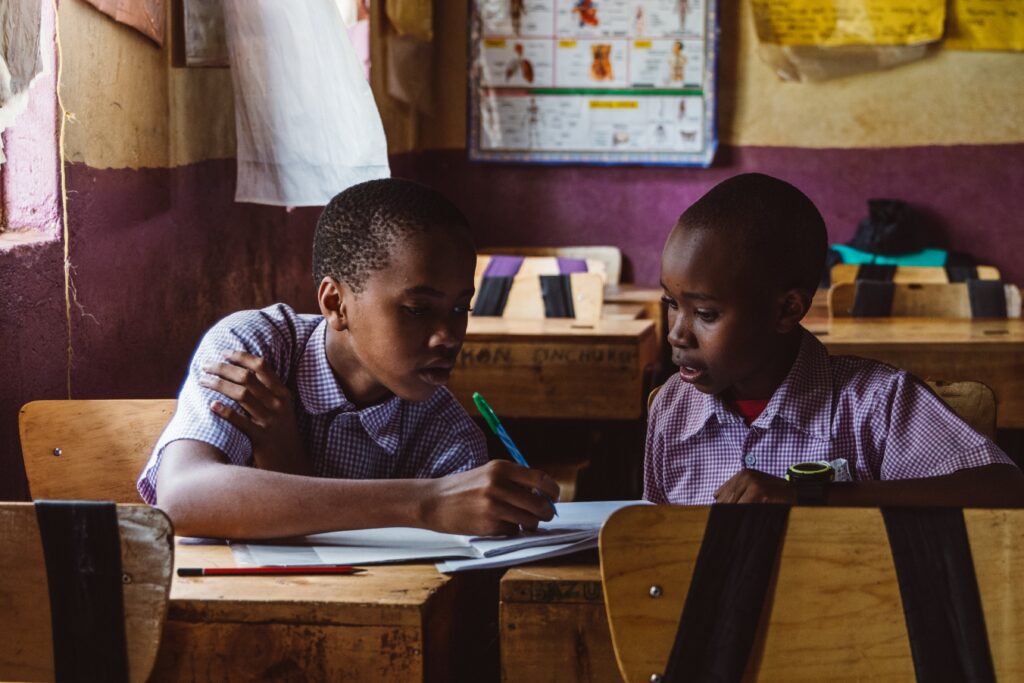 The image shows two kids from Africa studying at their school and discussing their classwork.