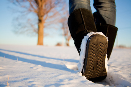 A person with black winter boots walking in snow.